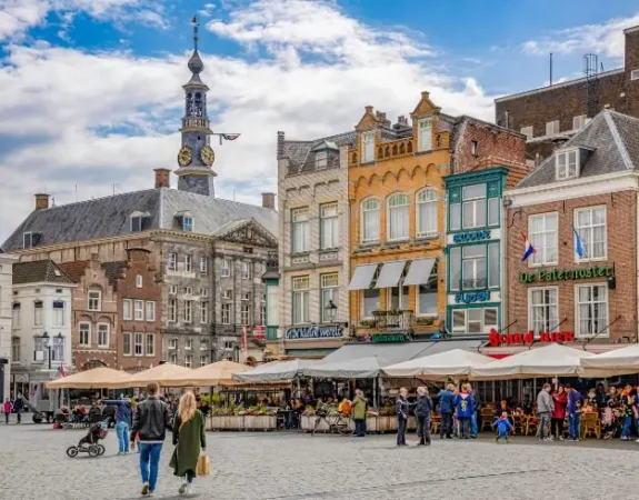 Colorful historic buildings and a lively outdoor café scene in the city center of Den Bosch, Netherlands.