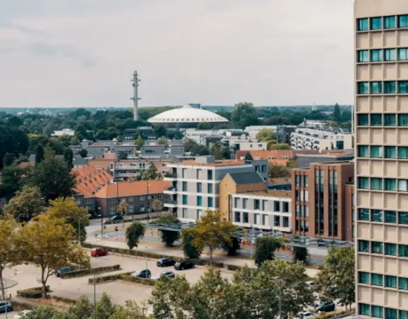 Cityscape of Eindhoven featuring modern buildings, residential areas, and the distinctive white Evoluon dome in the background.