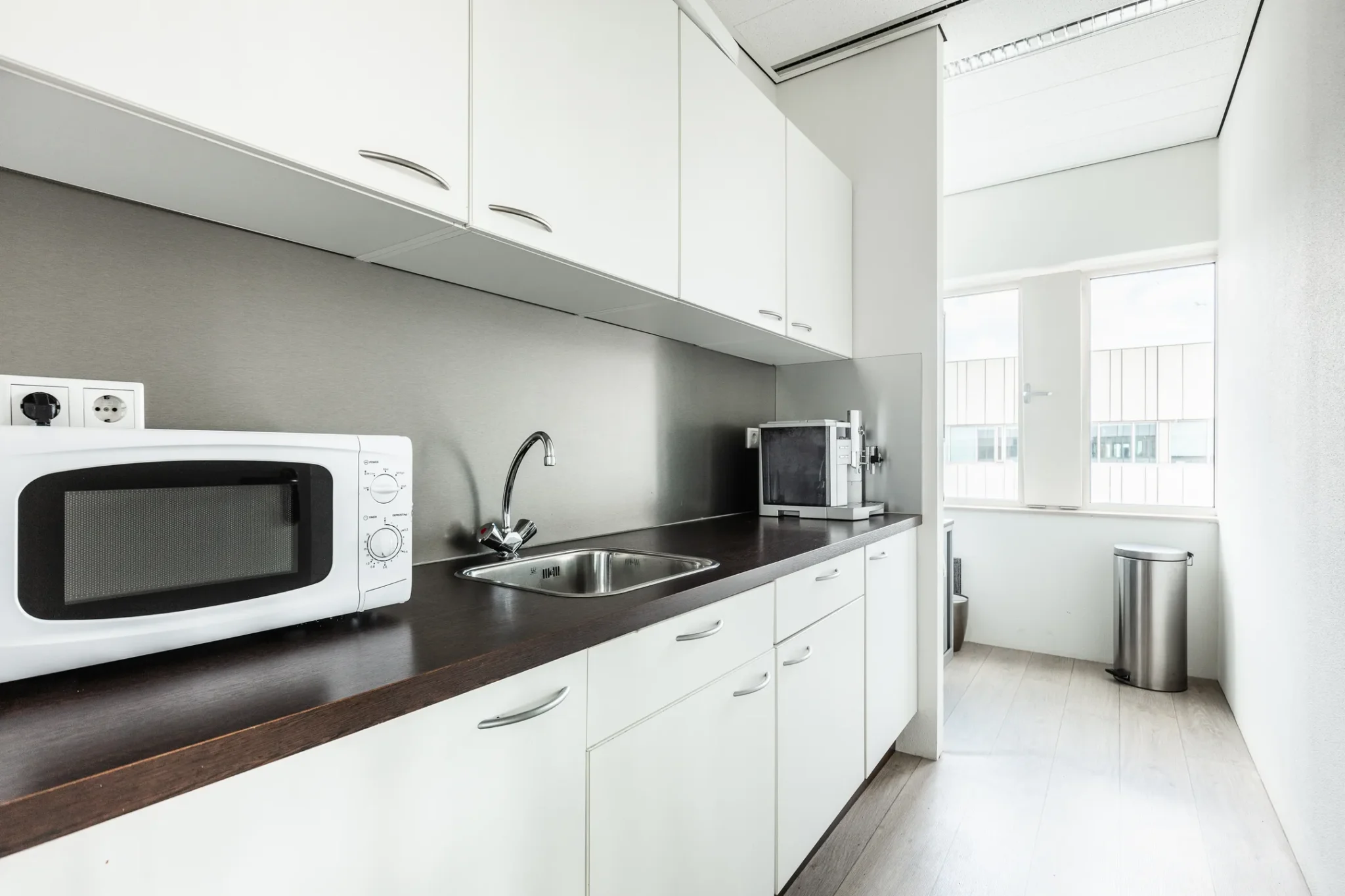 Moderne, smalle kitchenette in Herengracht 204 met witte kastjes, magnetrons en een roestvrijstalen wasbak.
