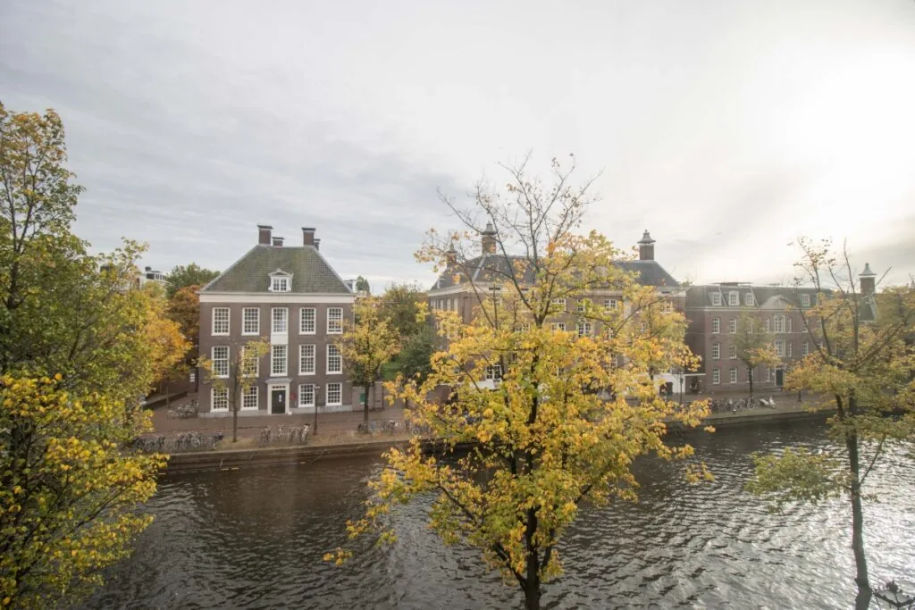 Herfstig uitzicht op het kantoor aan de Nieuwe Herengracht 4 in Amsterdam, gelegen aan een gracht met bomen en klassieke gevels.