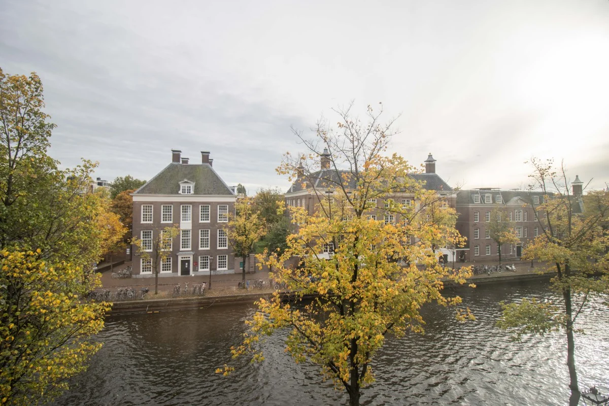 Herfstig uitzicht op het kantoor aan de Nieuwe Herengracht 4 in Amsterdam, gelegen aan een gracht met bomen en klassieke gevels.