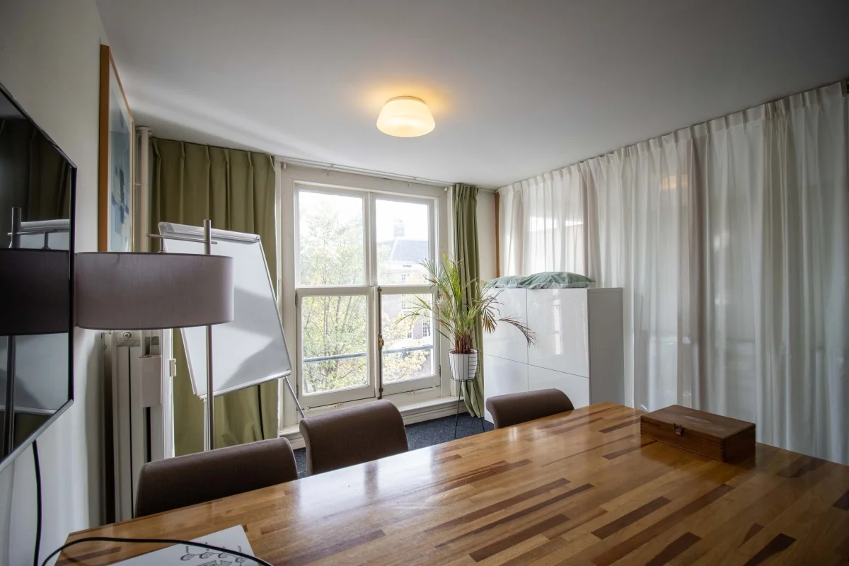 Vergaderruimte met houten tafel, flip-over en uitzicht op de gracht aan de Nieuwe Herengracht 6 in Amsterdam.