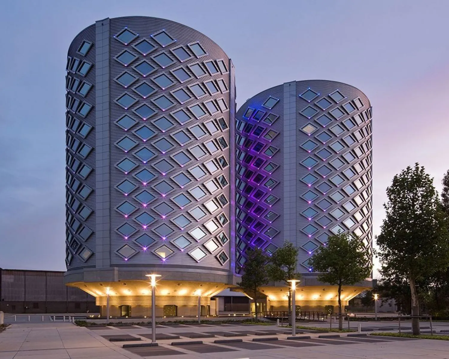 Twee futuristische kantoortorens van SugarCity aan de Ring in Halfweg, verlicht met paarse en blauwe accenten in de avondschemering.