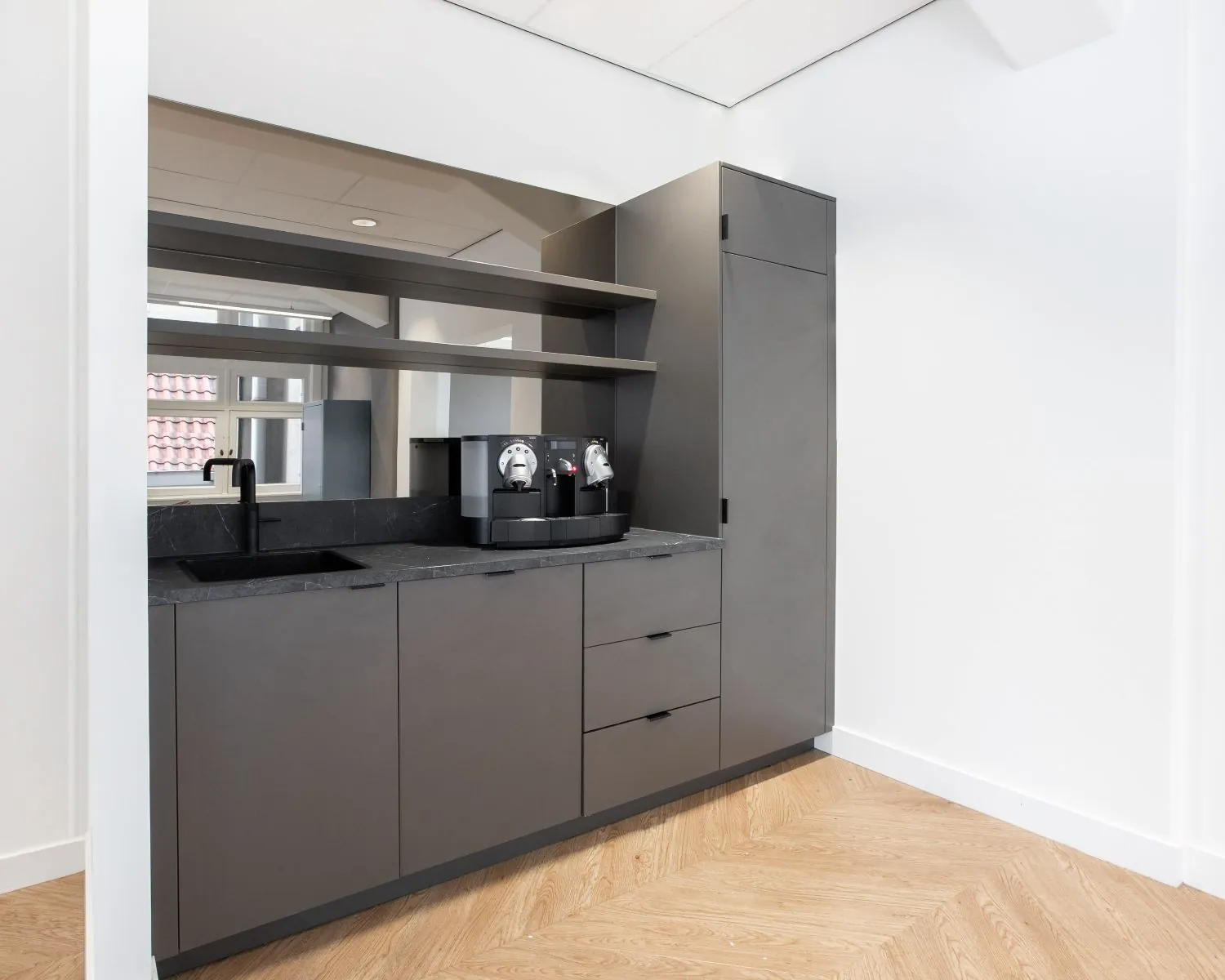 Moderne kantoorpantry met grijze kasten, zwarte kraan en een koffiezetapparaat in een kantoorruimte aan het Rokin in Amsterdam.