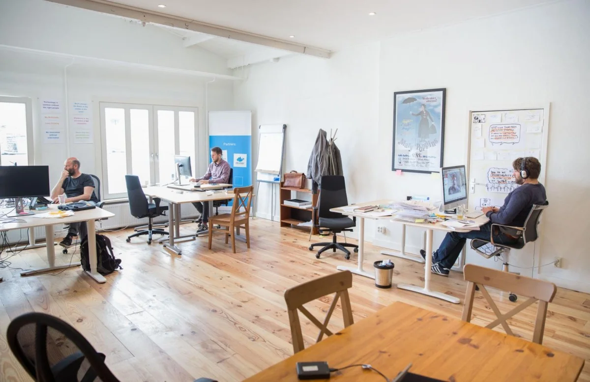 Moderne kantoorruimte met meerdere mensen aan het werk aan bureaus in een lichte omgeving.