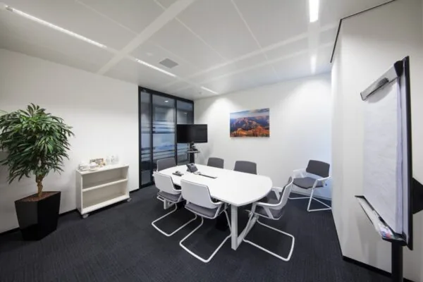 Moderne vergaderruimte aan de Strawinskylaan in Amsterdam met een ovale tafel, stoelen, een tv-scherm, een plant en een schilderij aan de muur.