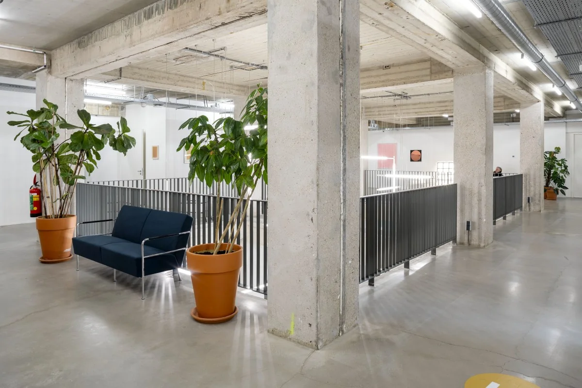 Moderne kantoorruimte met betonnen pilaren, een blauwe bank en grote planten in potten in Amsterdam Vijzelstraat 12.