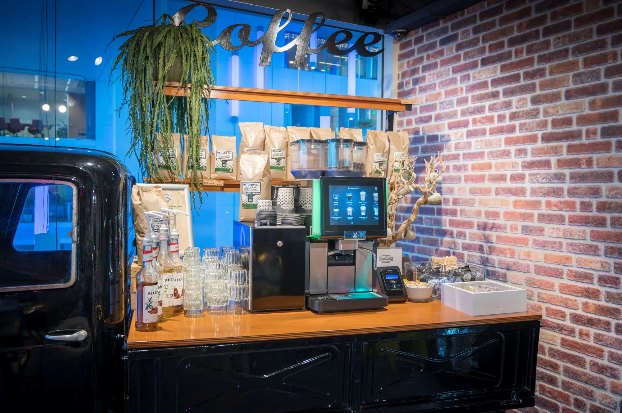 Koffiecorner met koffiemachine, siroopflessen en koffiebenodigdheden in kantoorruimte aan de Bargelaan 200 in Leiden.
