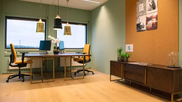 Moderne kantoorruimte aan de Bruistensingel 400 in Den Bosch met twee bureaus, gele bureaustoelen, stijlvolle verlichting en een houten kast tegen een kurkwand.