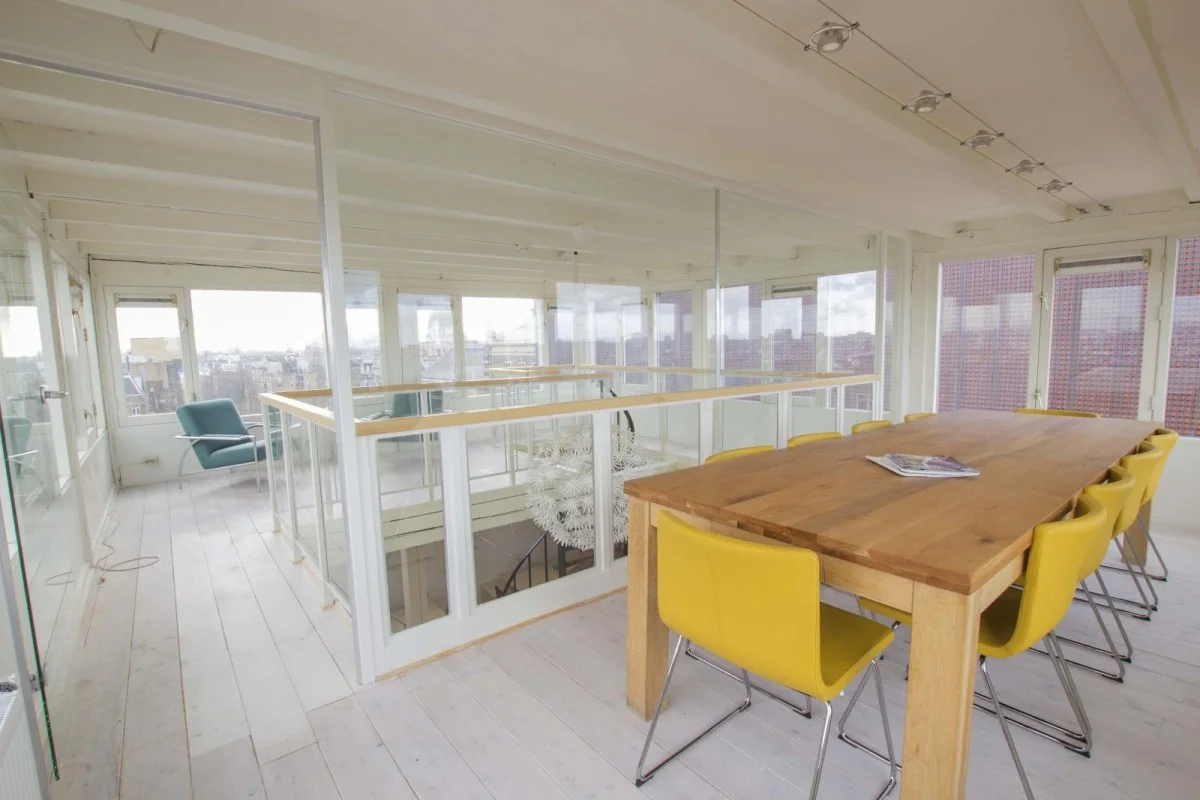 Een moderne kantoorruimte met een houten vergadertafel en gele stoelen in een lichte omgeving.