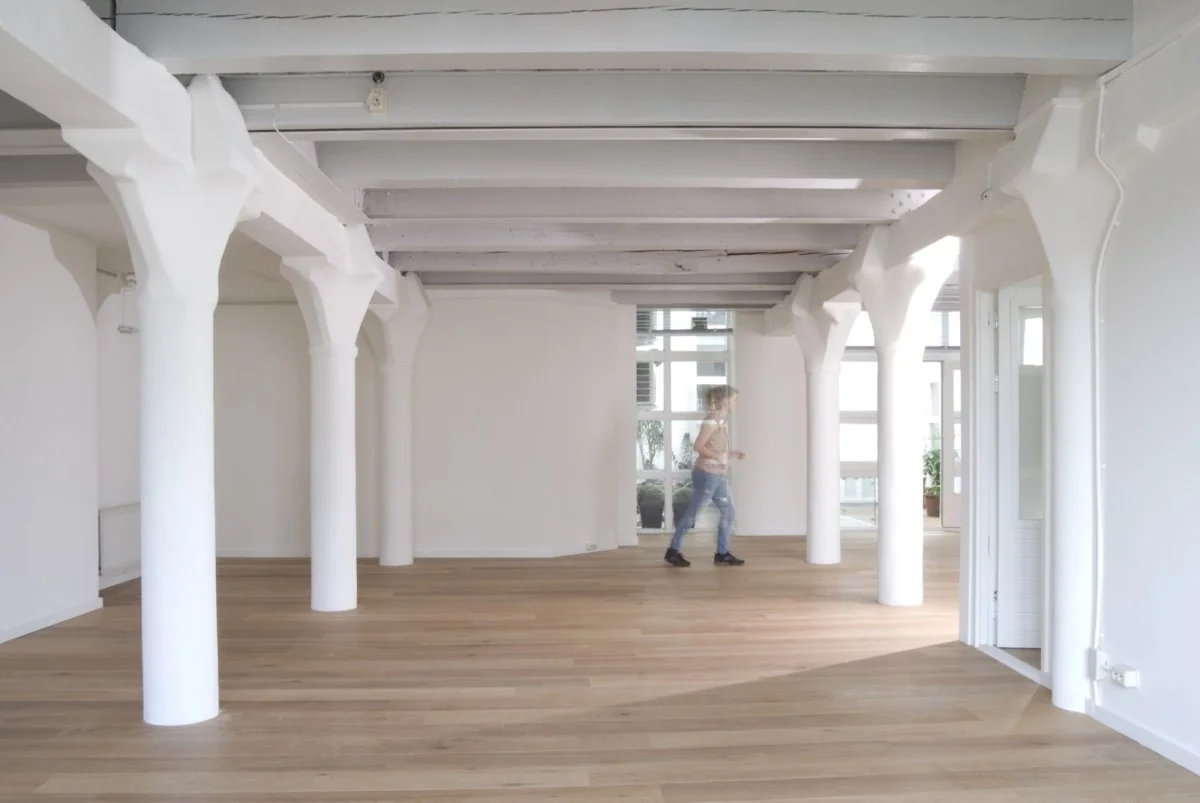 Lichte, lege kantoorruimte met houten vloer en witte steunpilaren aan de Korte Leidsedwarsstraat in Amsterdam.