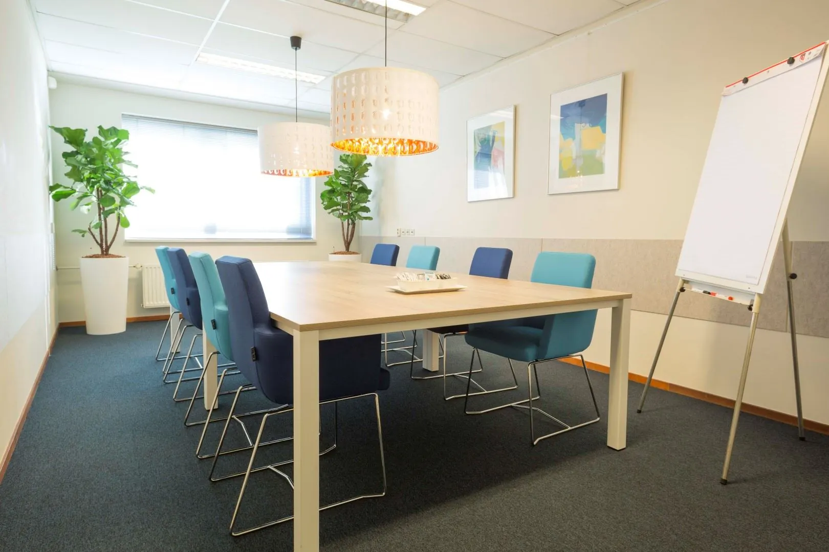 Vergaderruimte met moderne inrichting, blauwe stoelen, flip-over en grote ramen op Steenovenweg 5-9.