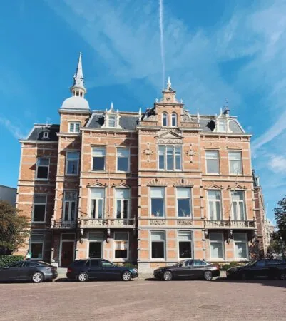 Groot, historisch bakstenen pand met torentje en versierde gevel onder een heldere blauwe lucht.