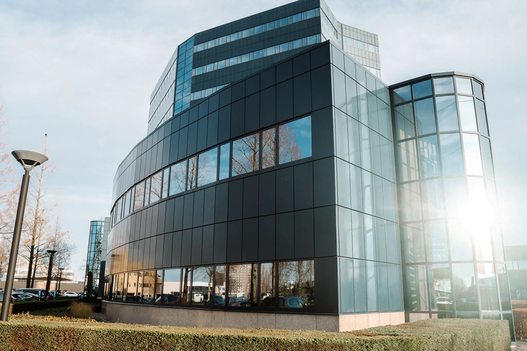Modern kantoorgebouw aan de Reitscheweg 1 in Den Bosch met glazen gevel en spiegelende ramen.