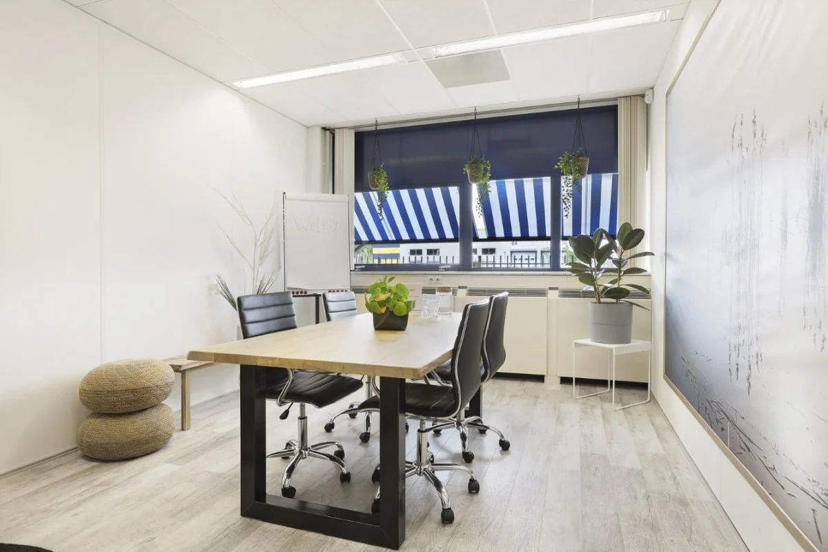 Moderne vergaderruimte in Markerkant, Almere met houten tafel, zwarte stoelen en grote ramen met blauw-witte zonwering.