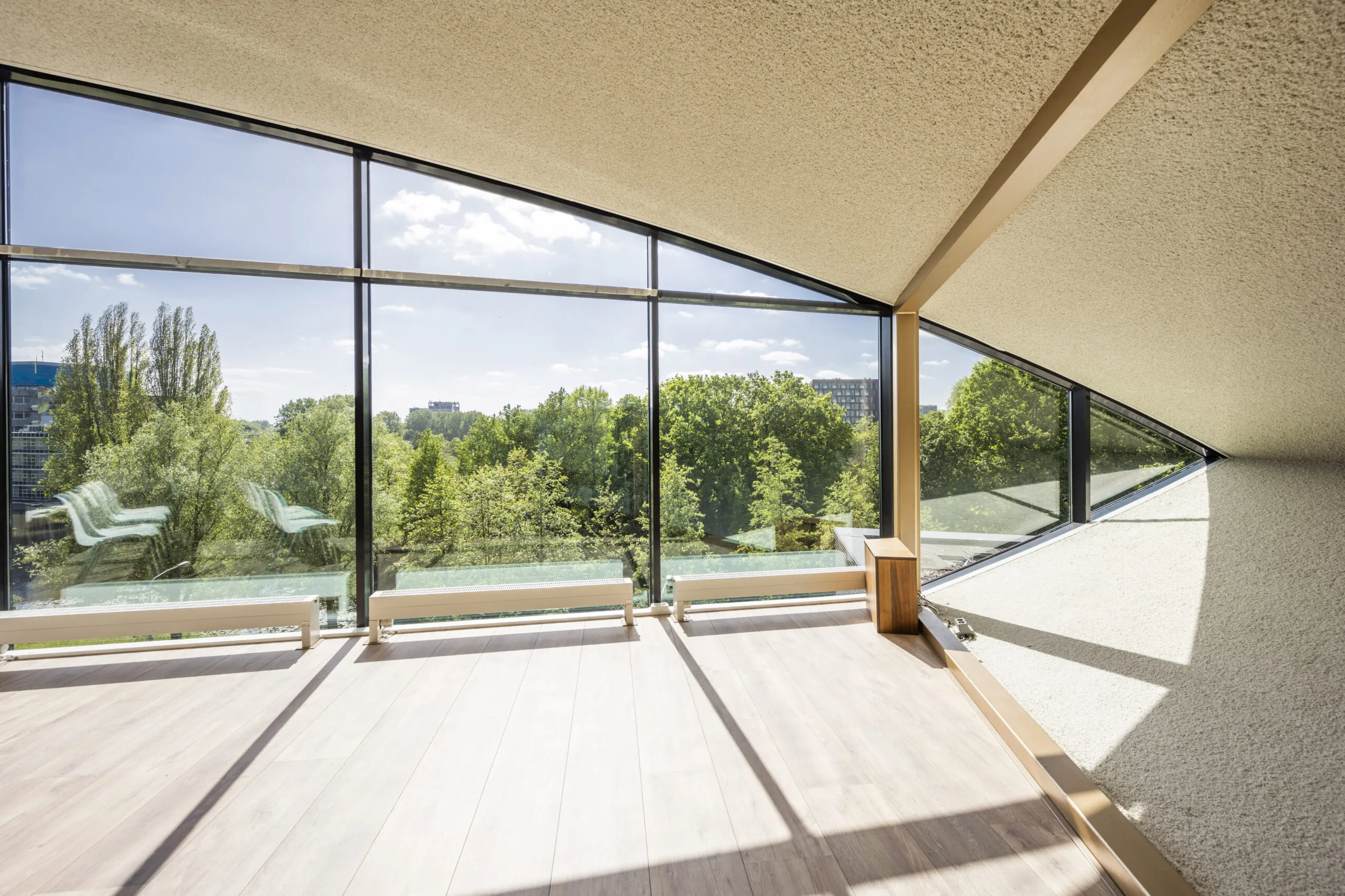 Een lichte kamer met grote ramen en uitzicht op een groene omgeving.