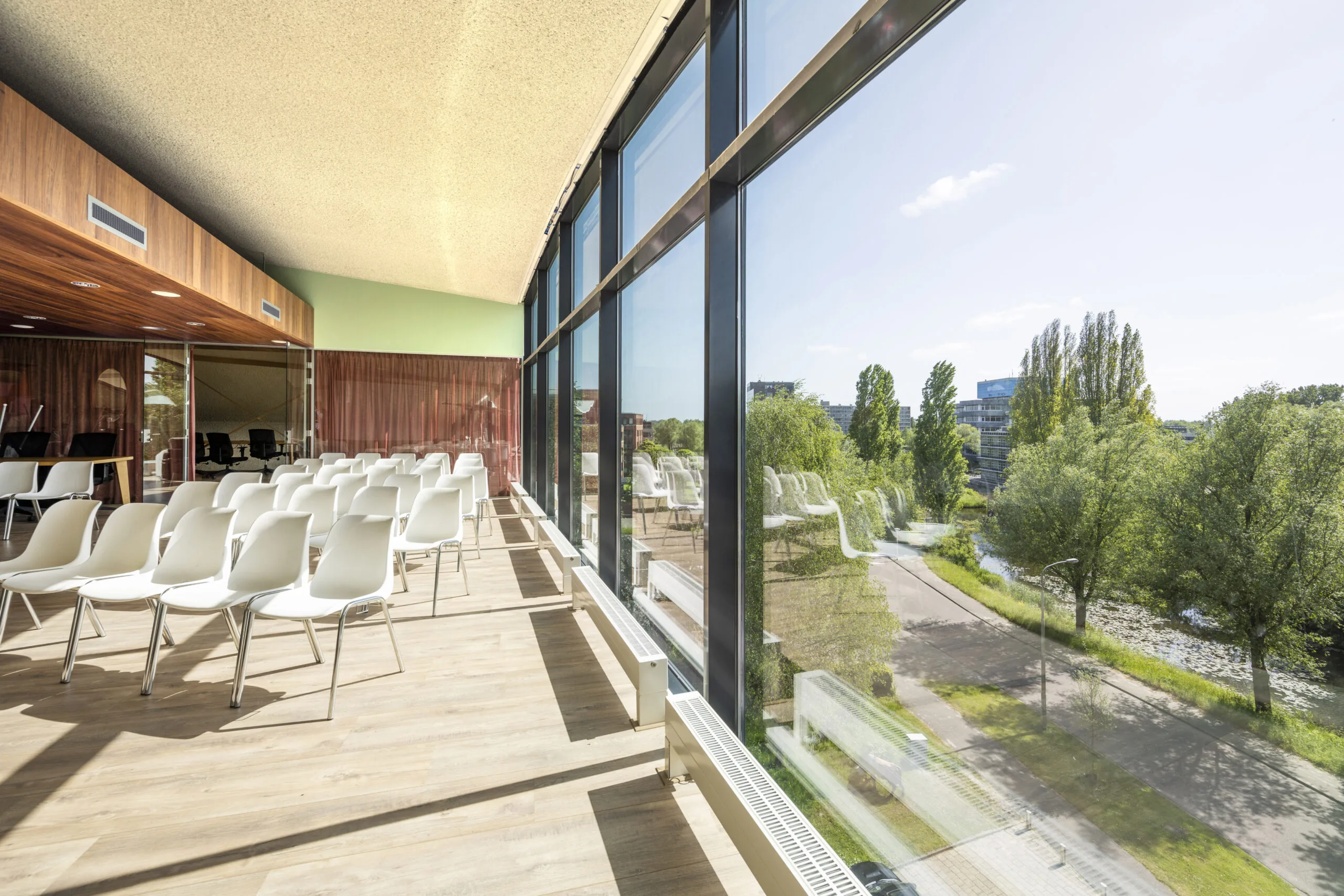 Een vergaderruimte met witte stoelen en grote ramen die uitzicht bieden op een groene omgeving.