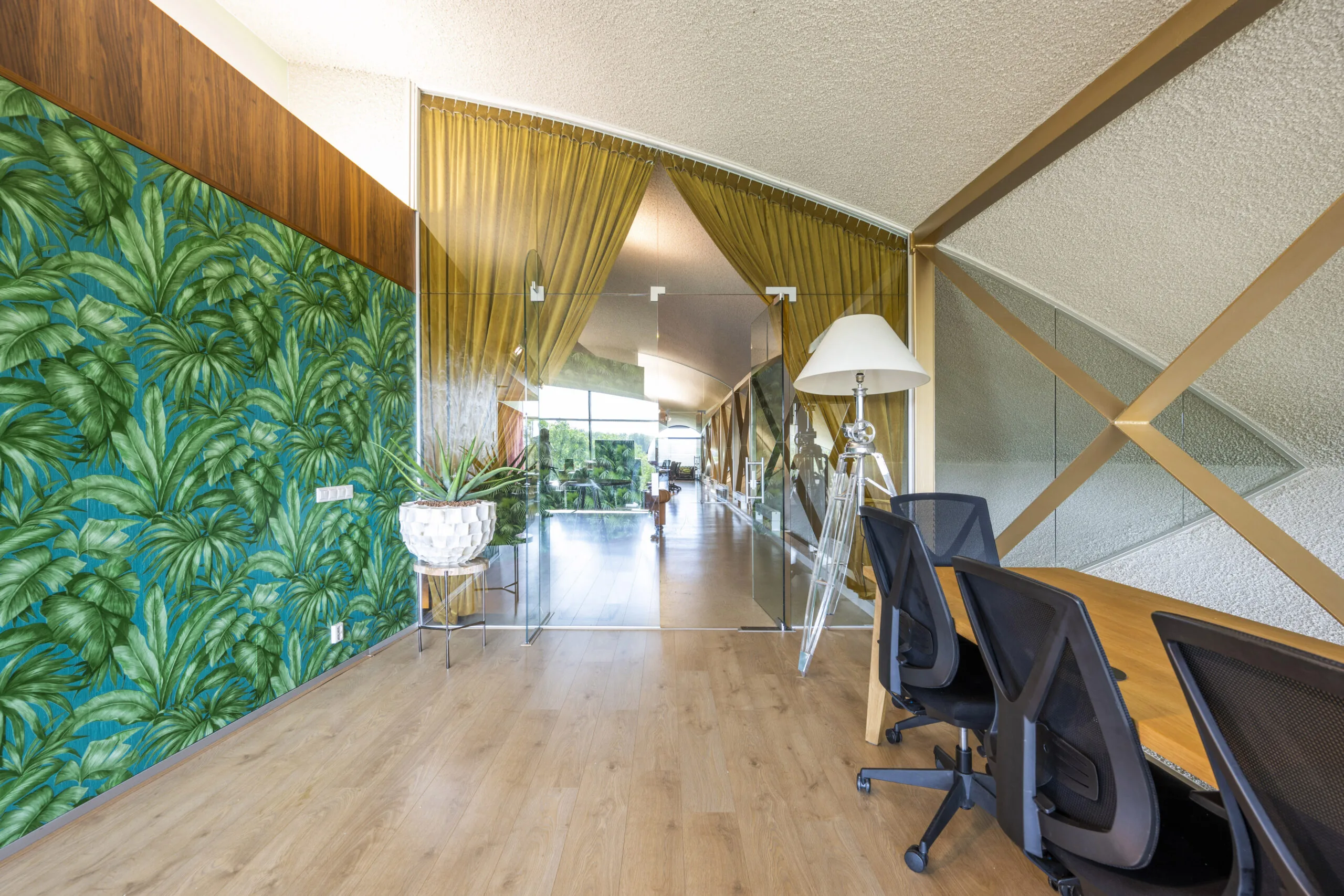Een moderne kantoorruimte met een plantenmotief op de muur, glazen deuren en houten meubels.