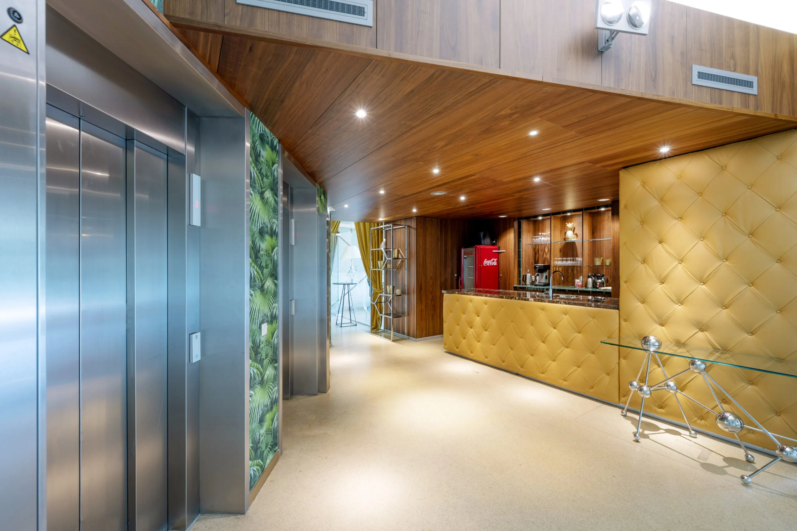 Een moderne ontvangsthal met een lift, een bar en decoratieve gele en houten elementen.
