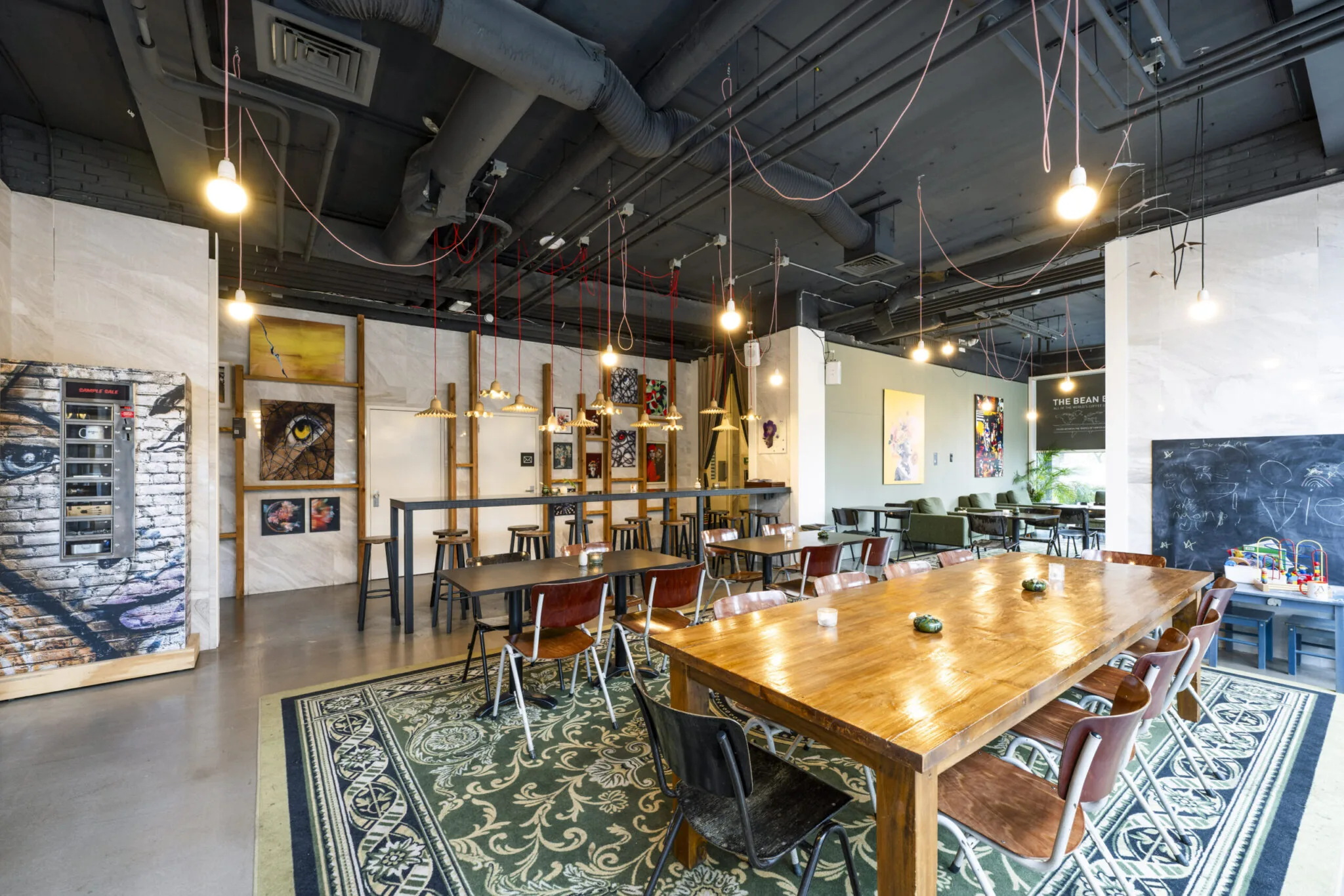 Modern ingerichte ontmoetingsruimte met houten tafels, kunst aan de muur en een speelhoek voor kinderen in Kronenburg, gefotografeerd door Paul Starink.
