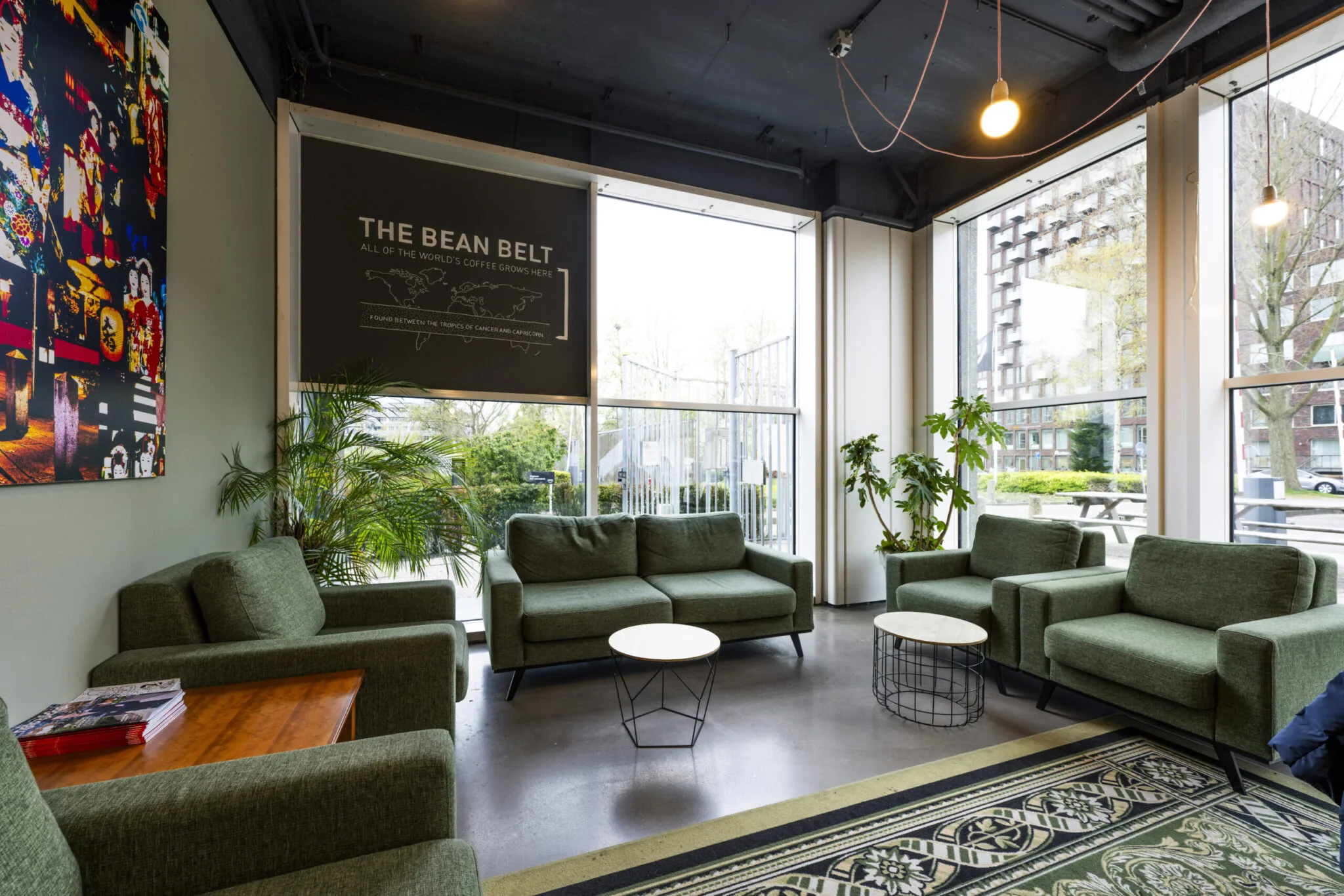 Moderne wachtruimte in Kronenburg 013 met groene fauteuils, grote ramen, planten en een muurposter over koffieproductie.