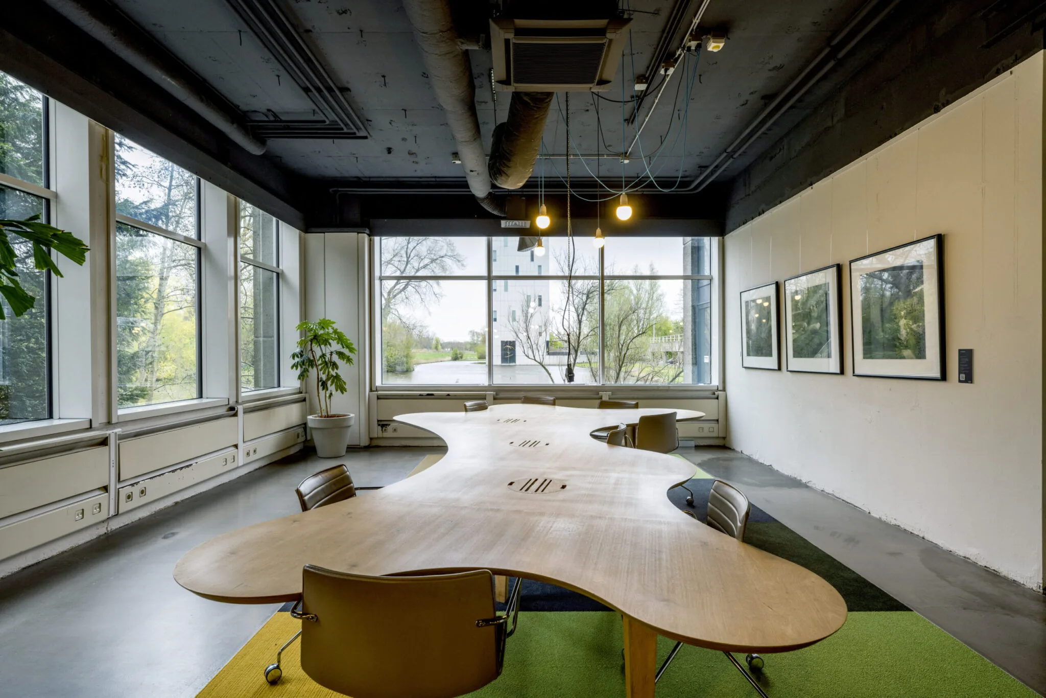 Vergaderruimte in Kronenburg 024 met golvend houten overlegtafel, moderne stoelen, grote ramen en kunst aan de muur.
