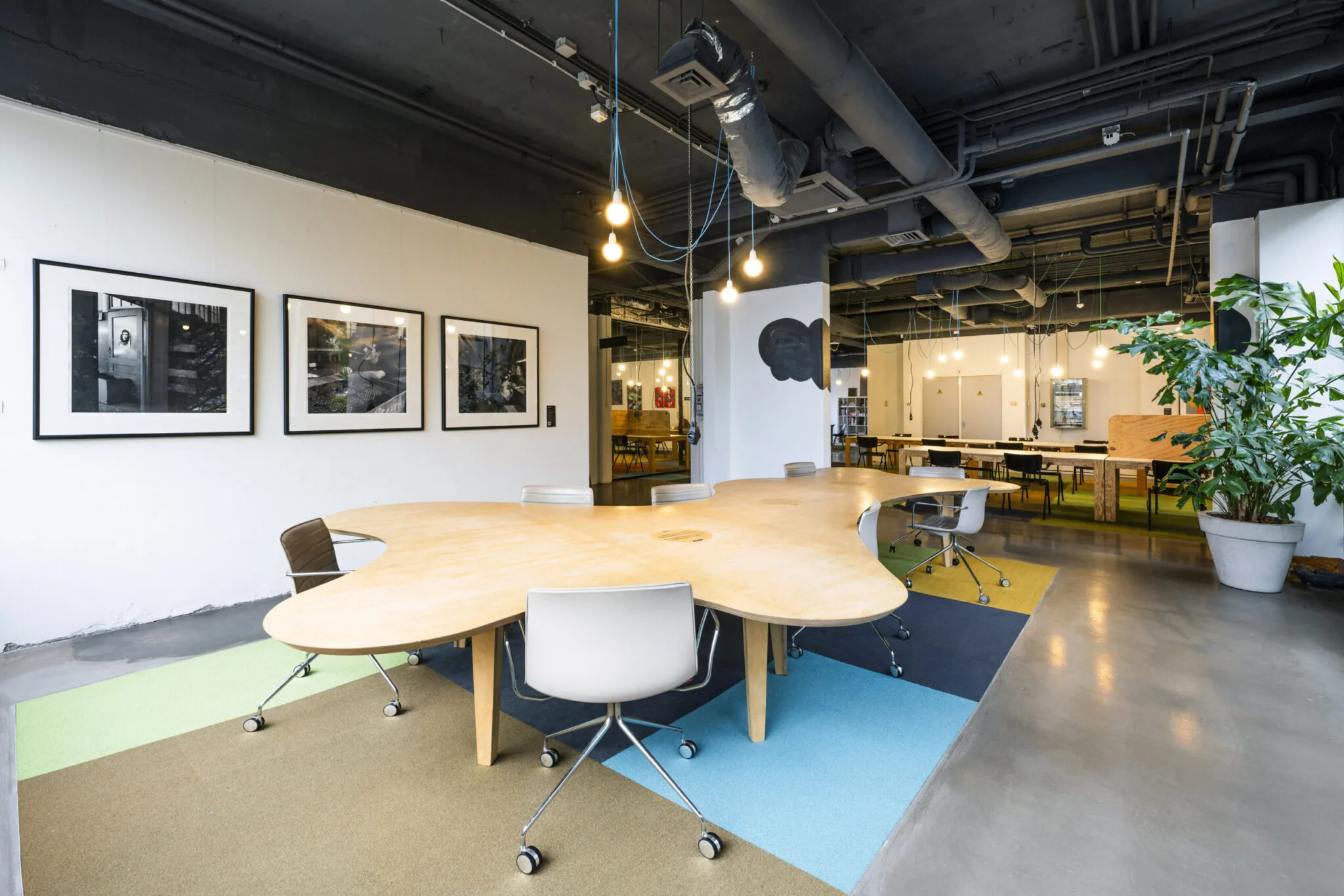 Moderne coworkingruimte in Kronenburg met een organisch gevormde houten tafel, bureaustoelen, kunst aan de muur en industriële plafonddetails.