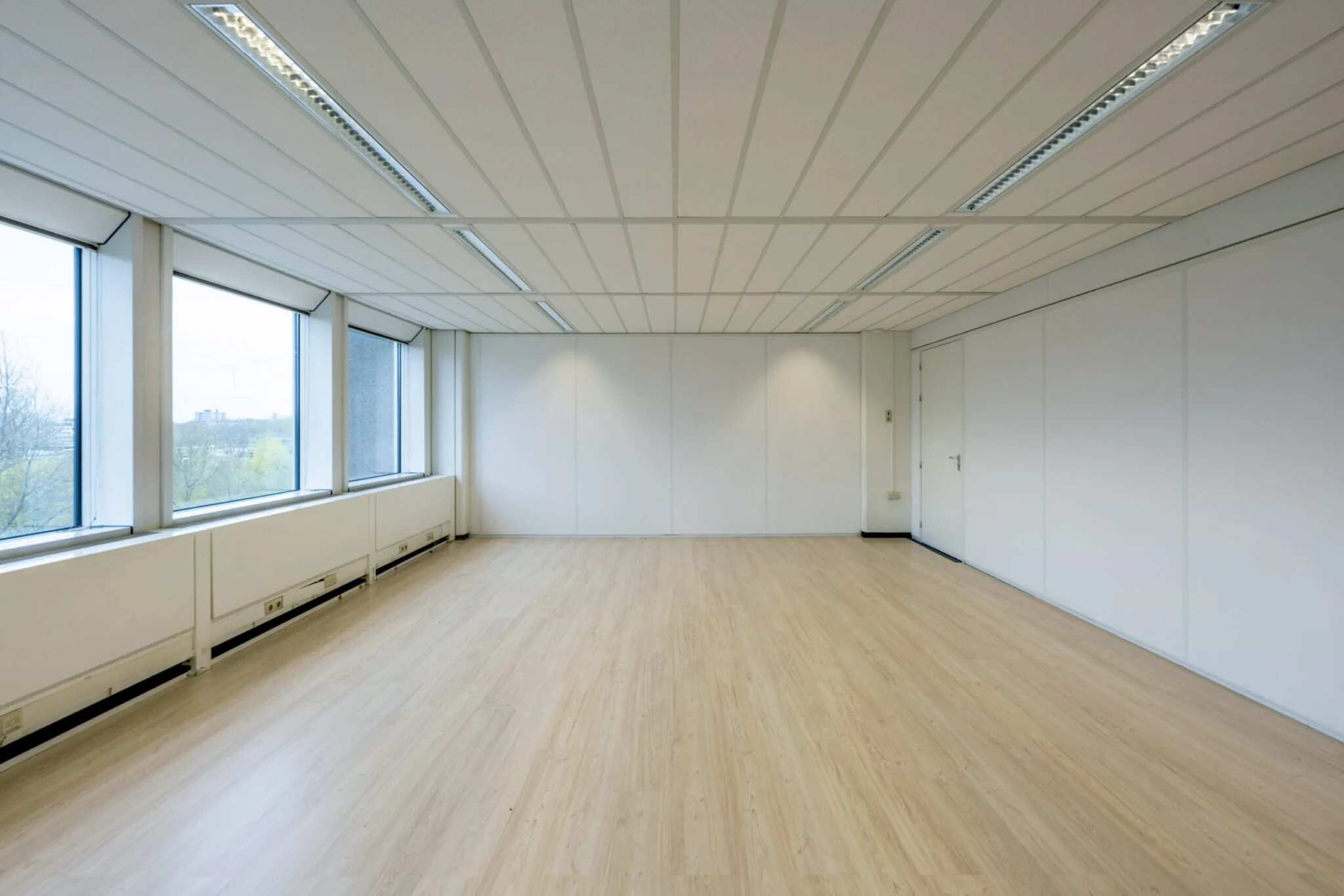 Lichte, lege kantoorruimte in Kronenburg met houten vloer, systeemplafond en grote ramen.