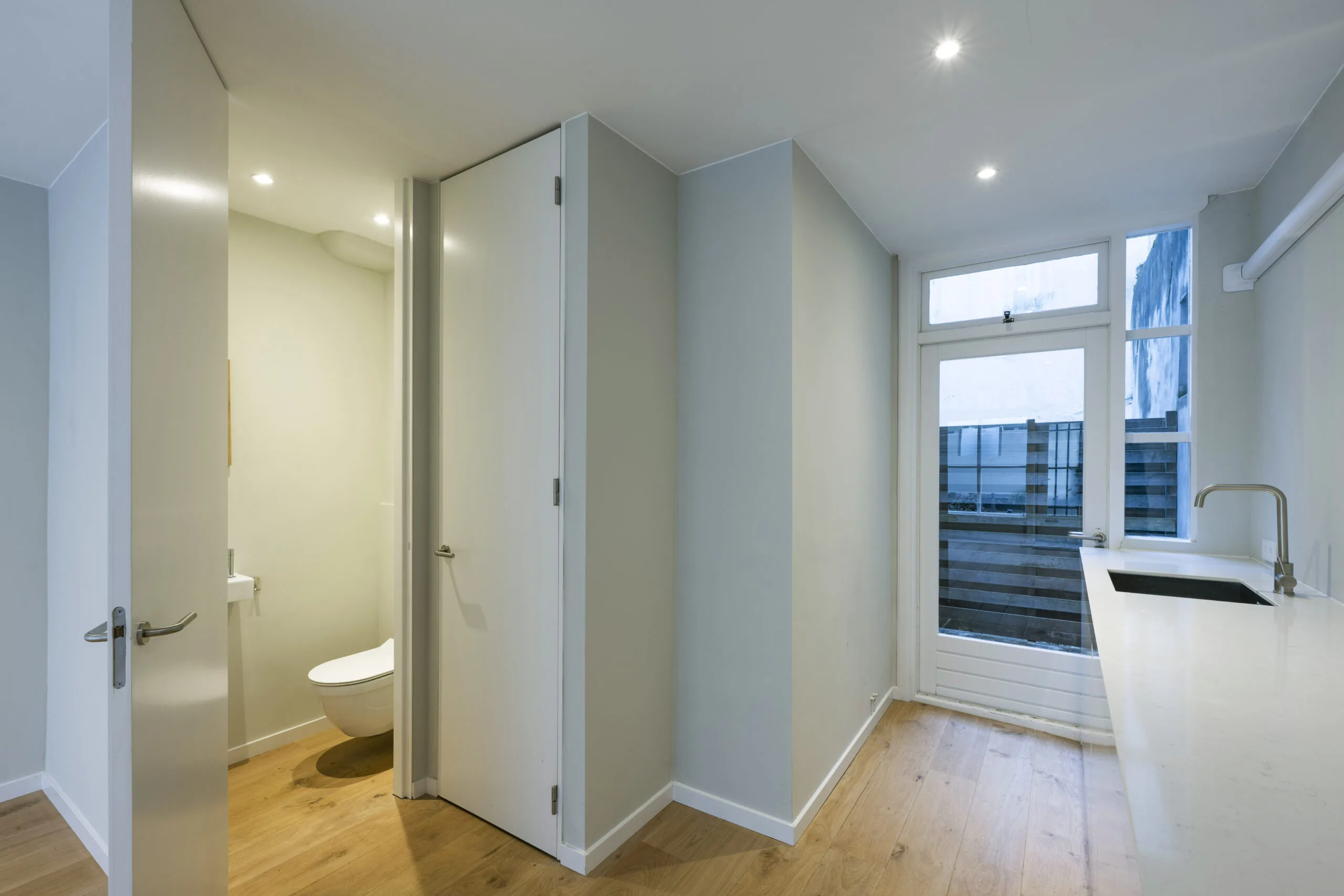 Moderne, smalle keuken met licht houten vloer, wit aanrechtblad en apart toilet in woning aan de Leliestraat.