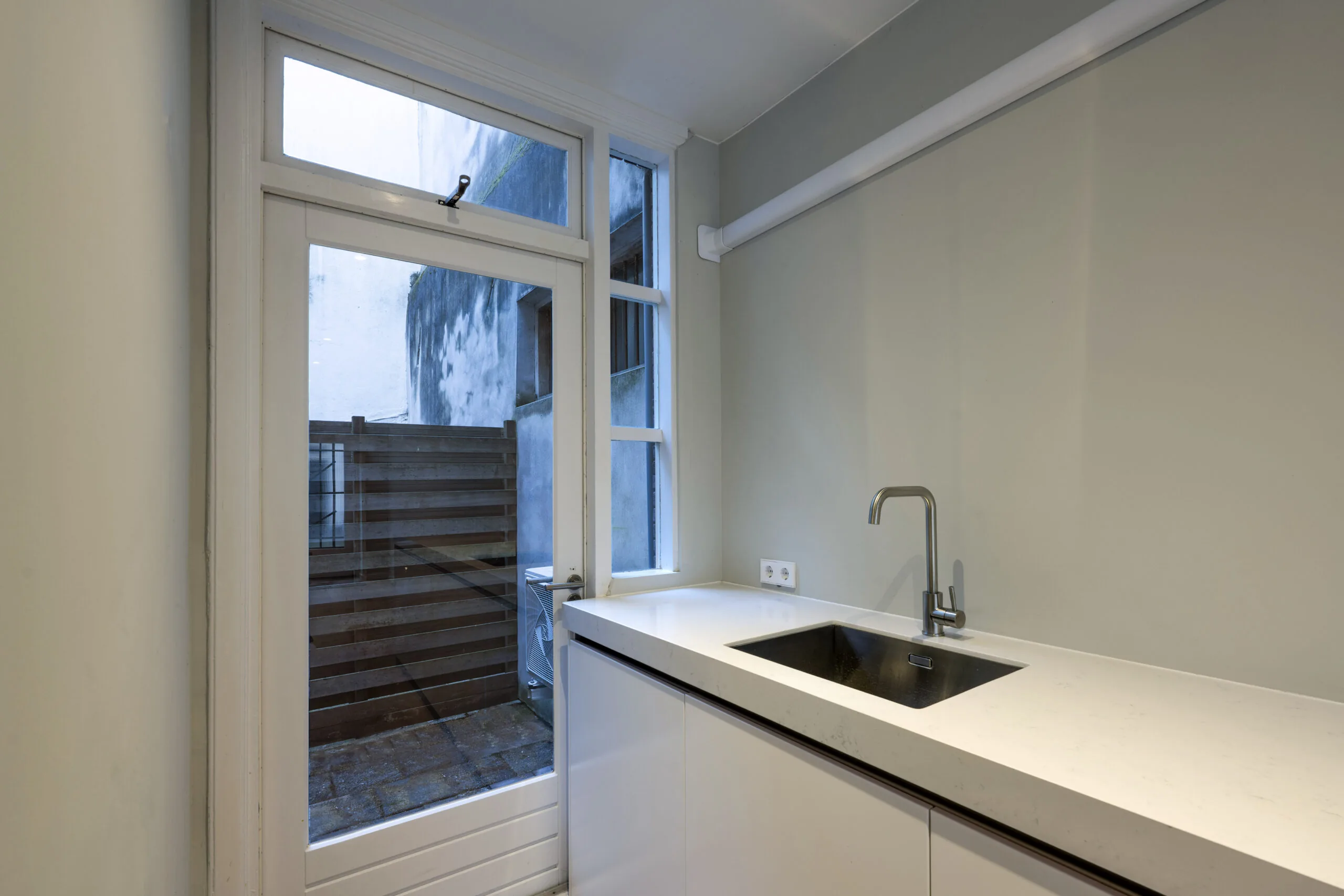 Moderne, minimalistische keuken met wit aanrechtblad en roestvrijstalen kraan aan de Leliestraat, met zicht op een kleine patio.