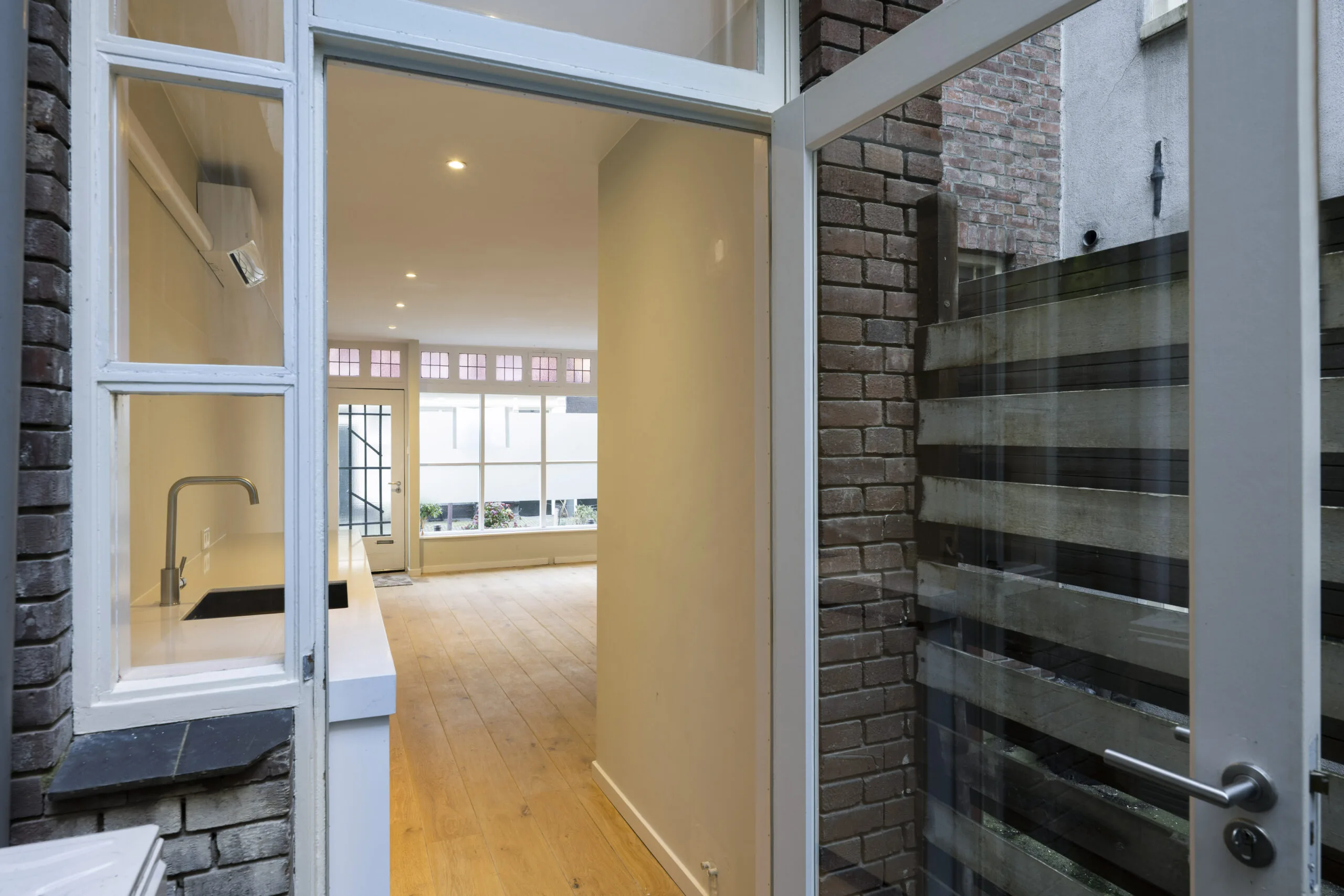 Doorkijk vanuit een kleine patio naar een lichte woonkamer met houten vloer aan de Leliestraat 024, ontworpen door Paul Starink.