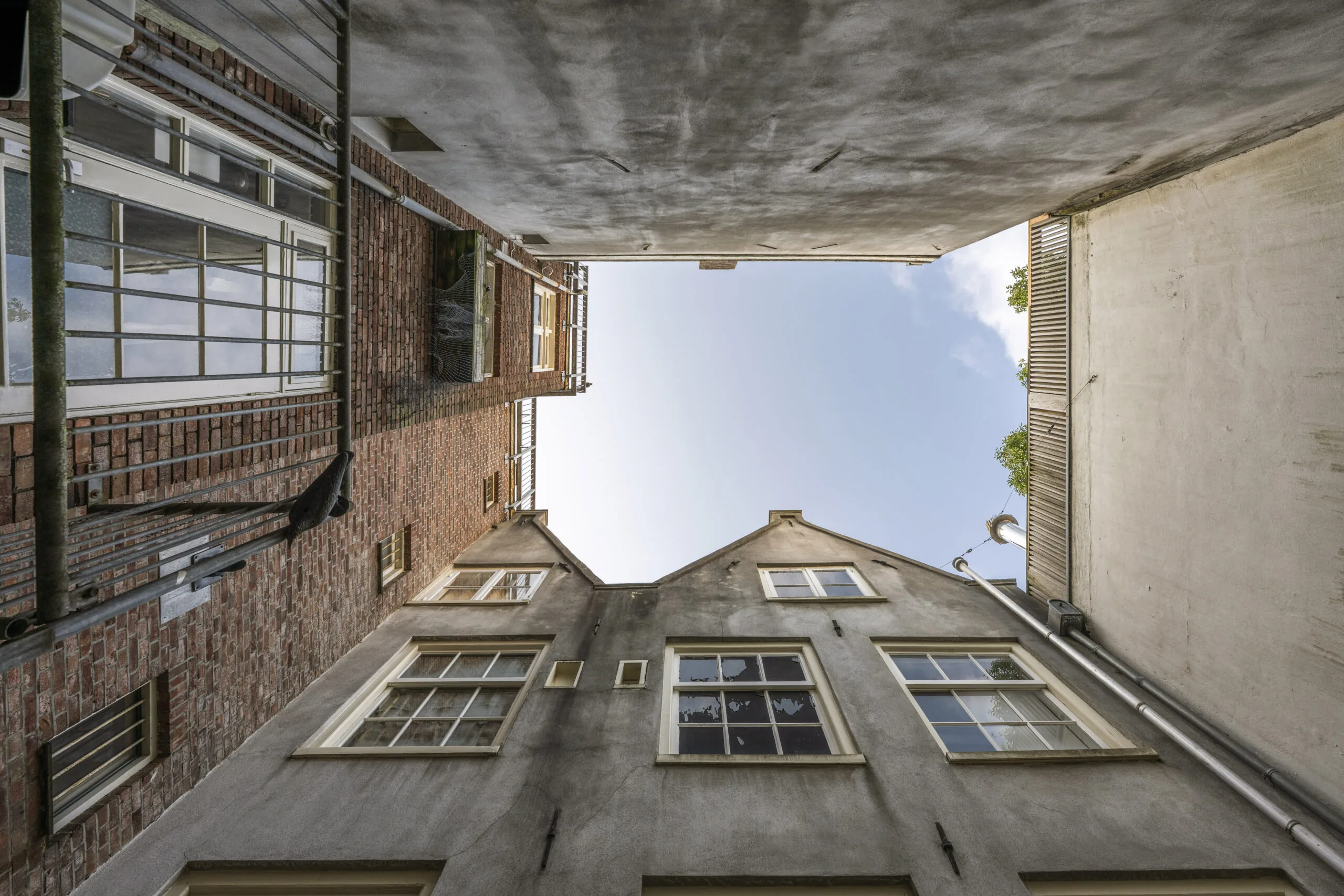 Kijk omhoog in een smalle steeg tussen oude gevels aan de Leliestraat, gefotografeerd door Paul Starink.