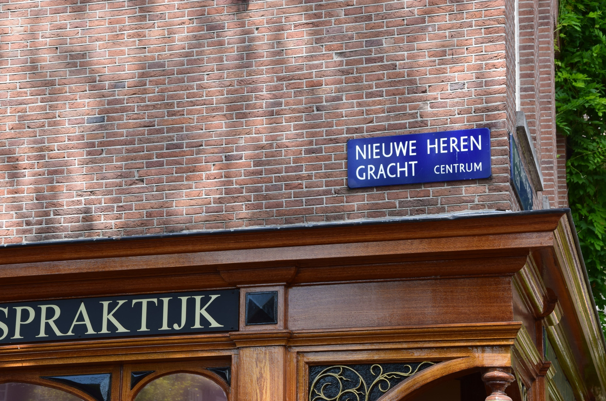 Straatnaambord "Nieuwe Herengracht Centrum" aan een bakstenen gevel boven een houten winkel- of praktijkpui.