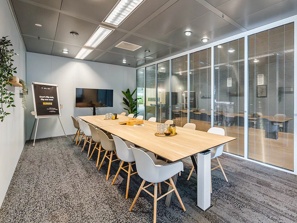 Vergaderzaal met een lange tafel, stoelen en een presentatiescherm.