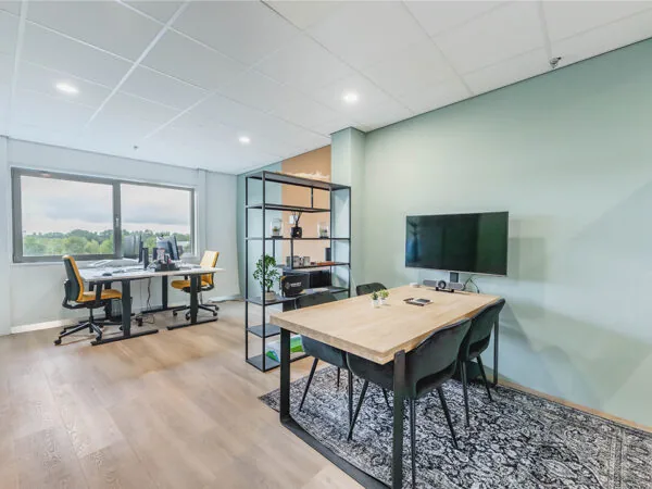 Een moderne kantoorruimte met bureaus, stoelen, een vergadertafel en een televisie aan de muur.