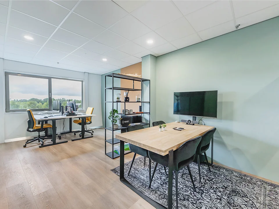 Een moderne kantoorruimte met bureaus, stoelen, een vergadertafel en een televisie aan de muur.