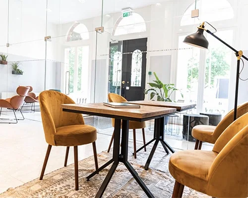 Kleine vergadertafel met vier mosterdgele stoelen in een moderne, lichte kantoorruimte.