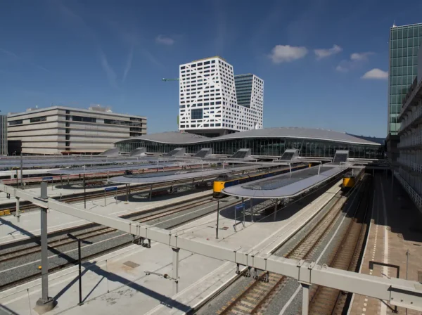 View of Utrecht Centraal railway station with modern architecture and multiple train tracks under a clear blue sky.