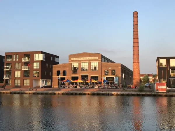Waterside view of the historic NV Draadbaan building with a tall brick chimney in Utrecht-Zuid during sunset.