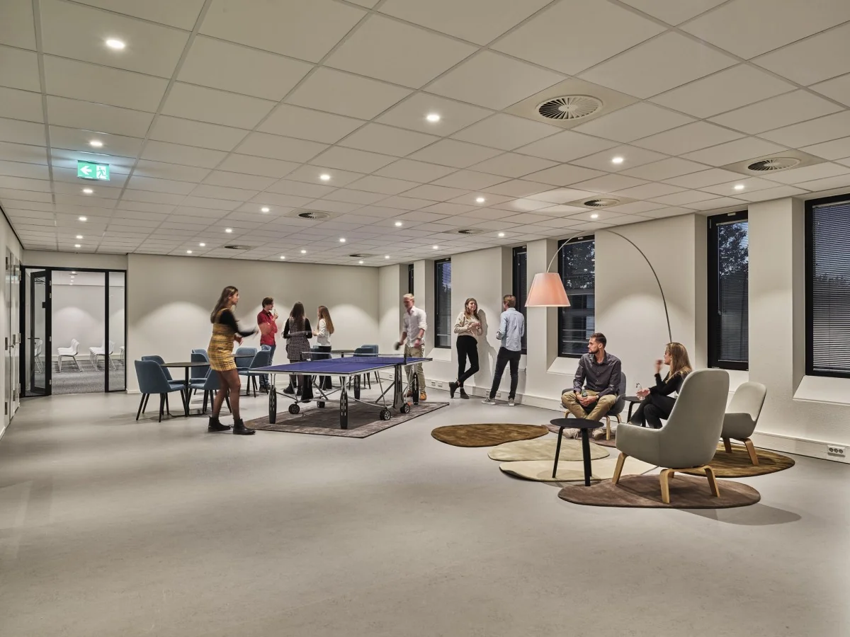 Moderne ontspanningsruimte in kantoorpand Van Deventerlaan 31-51 met mensen die tafeltennissen en loungen.