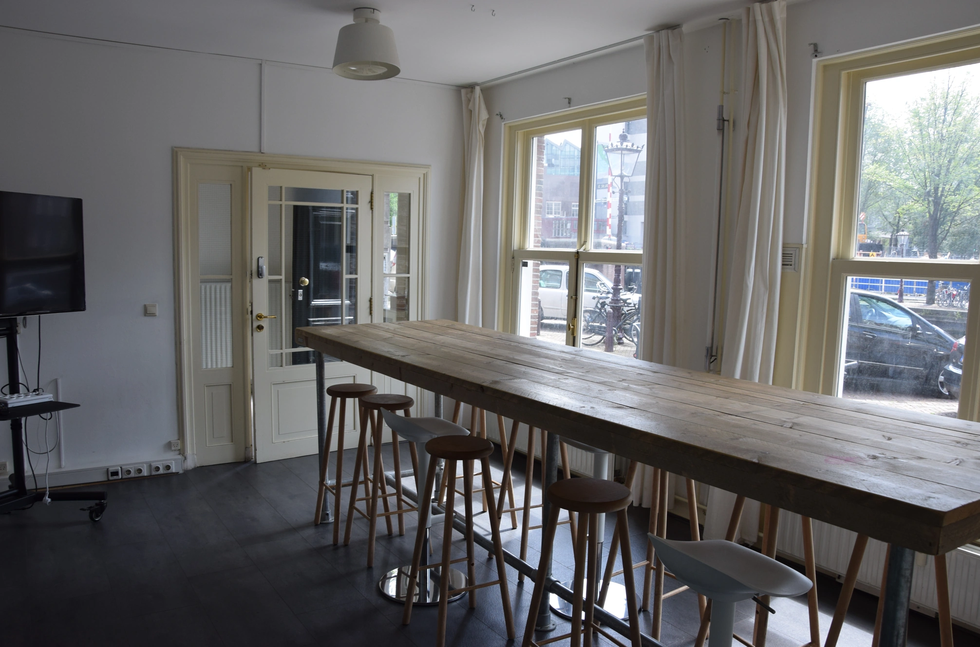 Vergaderruimte met een lange houten tafel, barkrukken en grote ramen die uitzicht bieden op de straat.