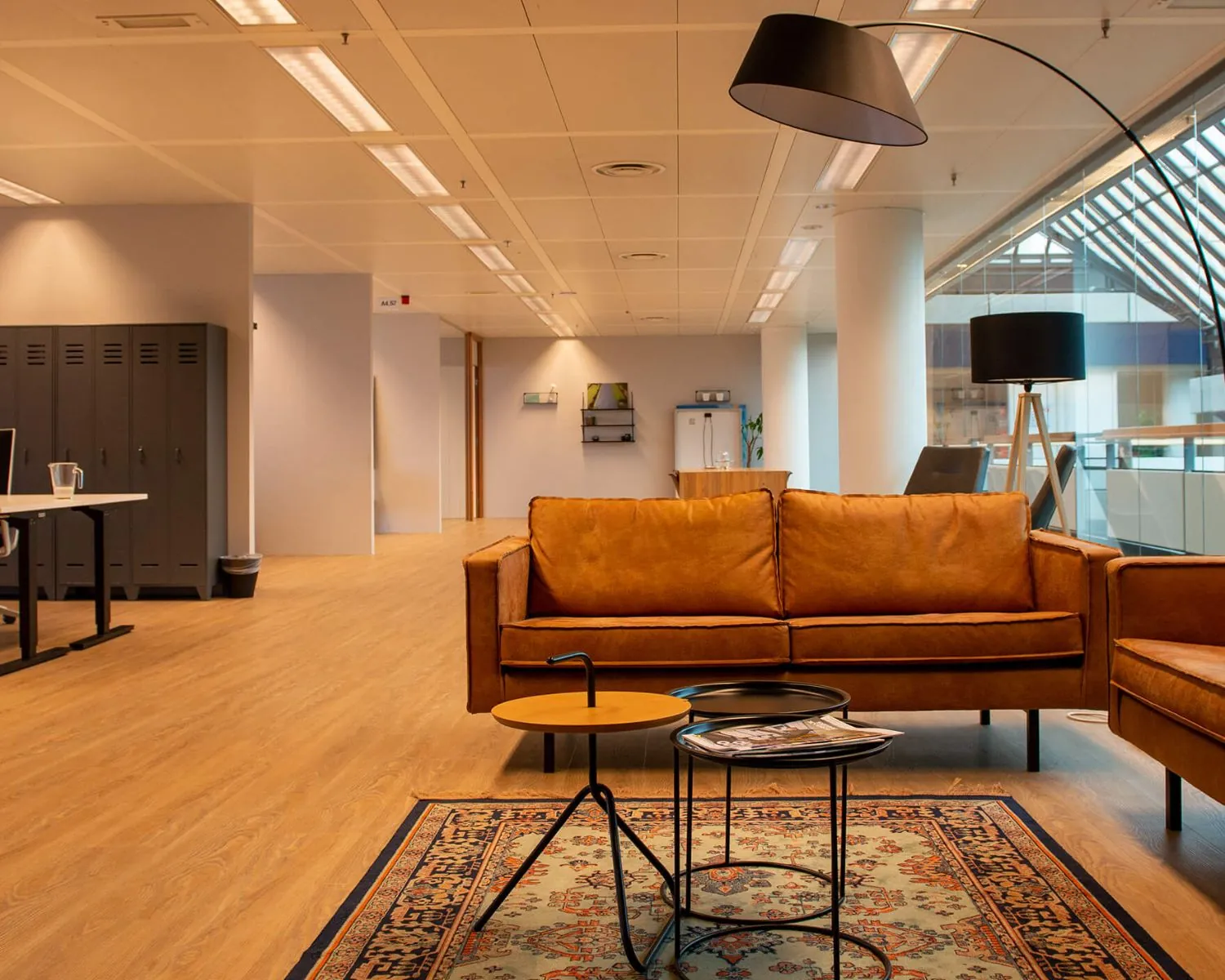 Moderne kantoorruimte met een bruine leren zithoek, vloerkleed en designverlichting.