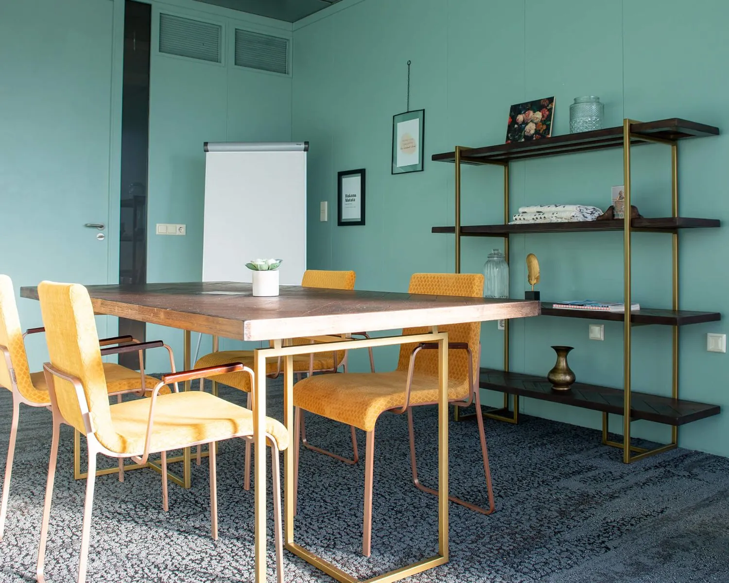 Vergaderruimte met een houten tafel, gele stoelen, flip-over en wandrek tegen een mintgroene muur.